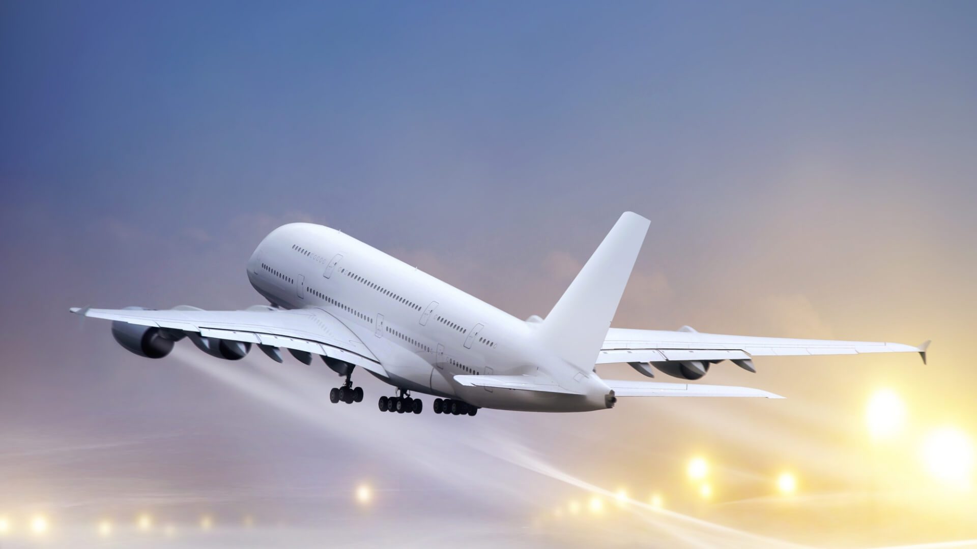 Afuzion : A large white airplane with four engines taking off from a runway with lights visible in the background.